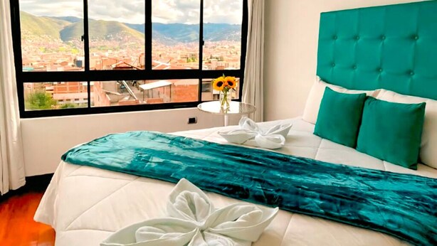 Camera d'albergo con un letto, vista sulla città attraverso ampie finestre e un poggiatesta verde.