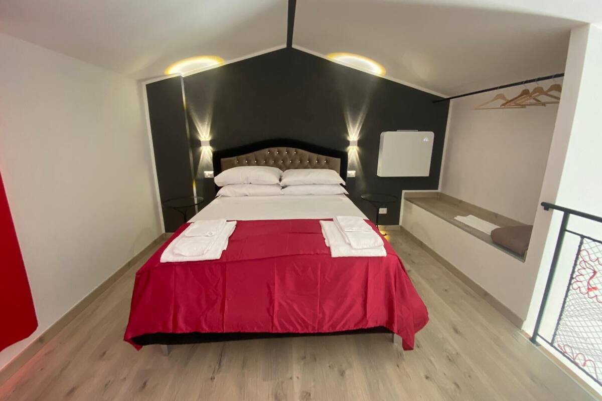 A hotel room with a large bed, a red bedspread, and two bedside lamps.