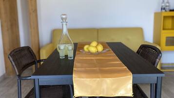 A dining table with a bottle and lemons, surrounded by wicker chairs, in a room with a wooden ceiling and a yellow wall.