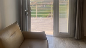 A room with a beige sofa, a sliding glass door leading to a balcony with a view of a green landscape and distant buildings. - Dimora Filippo (Sant'Elpidio a Mare)
