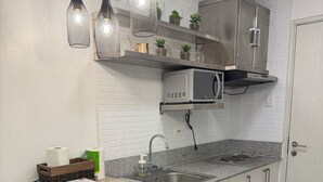 Una cucina compatta con forno a microonde integrato, lavello e un piccolo frigorifero. Sono presenti due sgabelli di legno e un tavolino con piano di lavoro.
