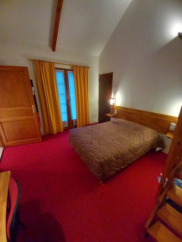 A hotel room with a large bed, wooden headboard, a nightstand, a desk, and a wardrobe. - Le motel st Martin (Verneuil d'Avre et d'Iton)