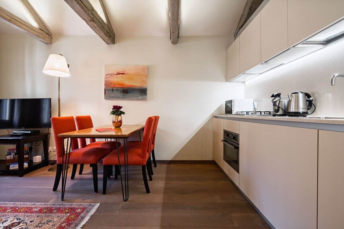 A compact kitchen with a dining area, a flat-screen TV, and a painting on the wall.