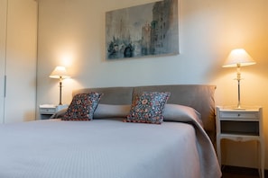 A neatly made bed with floral pillows, a painting on the wall, and two bedside lamps. - Ca' Barbarina 2 (Venezia)