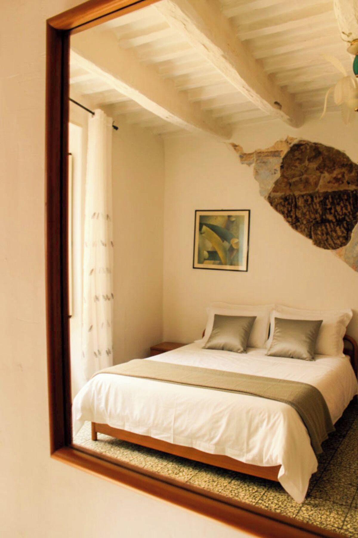 A bedroom with a bed, a painting, and a stone wall.