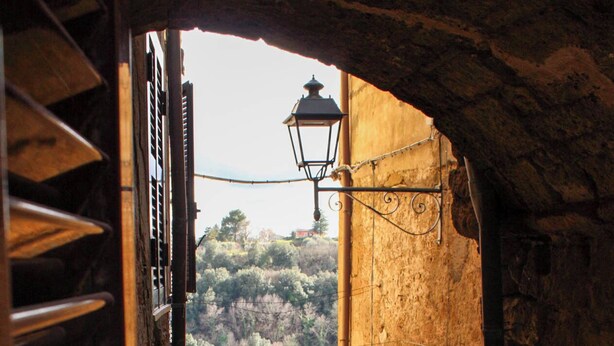 A narrow stone staircase leading to a building with a tiled roof, a lantern, and a view of a hillside. - Pitigliano Historic Center (Pitigliano)