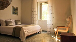 A bedroom with a bed, a chair, a window with curtains, and a painting on the wall. - Pitigliano Historic Center (Pitigliano)
