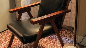 A chair with a wooden frame and black seat, positioned near a window with patterned wallpaper. - Pitigliano Historic Center (Pitigliano)