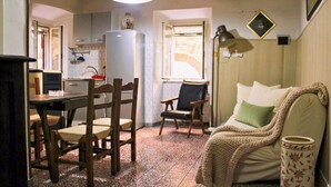 A cozy kitchen with wooden chairs, a dining table, and a refrigerator. There is a window providing natural light and a lamp on the table. - Pitigliano Historic Center (Pitigliano)
