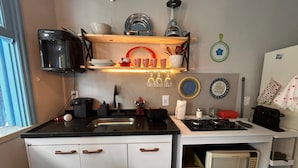A compact kitchen with a sink, stove, microwave, and shelves with dishes and utensils. - Flor e Fruto Retreat - Little Flower House (Rio de Janeiro)