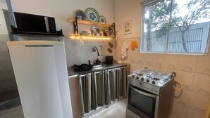 A compact kitchen with a refrigerator, stove, and sink. There is a window with a view of trees and a fence. - Flor e Fruto Retreat - Little Fruit House (Rio de Janeiro)