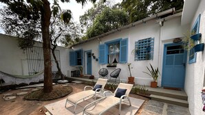 A white building with blue shutters and a door, a hammock, and two lounge chairs with cushions. - Flor e Fruto Retreat - Little Fruit House (Rio de Janeiro)