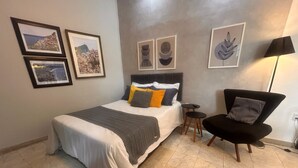 A bedroom with a bed, a chair, a small table, and wall art. - Flor e Fruto Retreat - Little Fruit House (Rio de Janeiro)