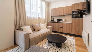 Ein modernes Wohnzimmer mit einer Couch, einem Couchtisch und einer Küchenzeile mit Holfschränken und einem eingebauten Backofen.