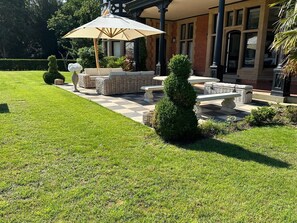 A well-maintained outdoor patio area with wicker furniture, a stone table, and a large umbrella. - The Manor Herringswell (Bury St Edmunds)