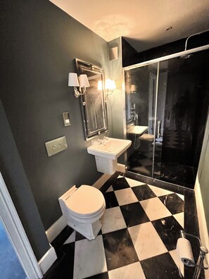 A bathroom with a black and white checkered floor, a white toilet, a sink, and a mirror with wall sconces. - The Manor Herringswell (Bury St Edmunds)