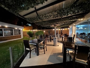 An outdoor dining area with tables and chairs, a brick wall, and a green lawn.