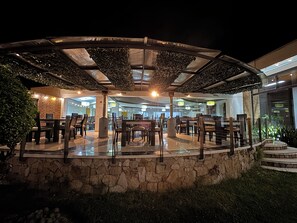 An outdoor dining area with stone walls, tables, and chairs, surrounded by greenery and a covered section. - D'Acosta Hotel Belencito (Nobsa)