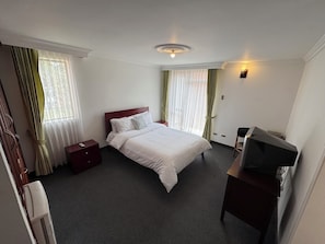 A hotel room with a bed, a desk with a computer, a nightstand, and a window with curtains. - D'Acosta Hotel Belencito (Nobsa)