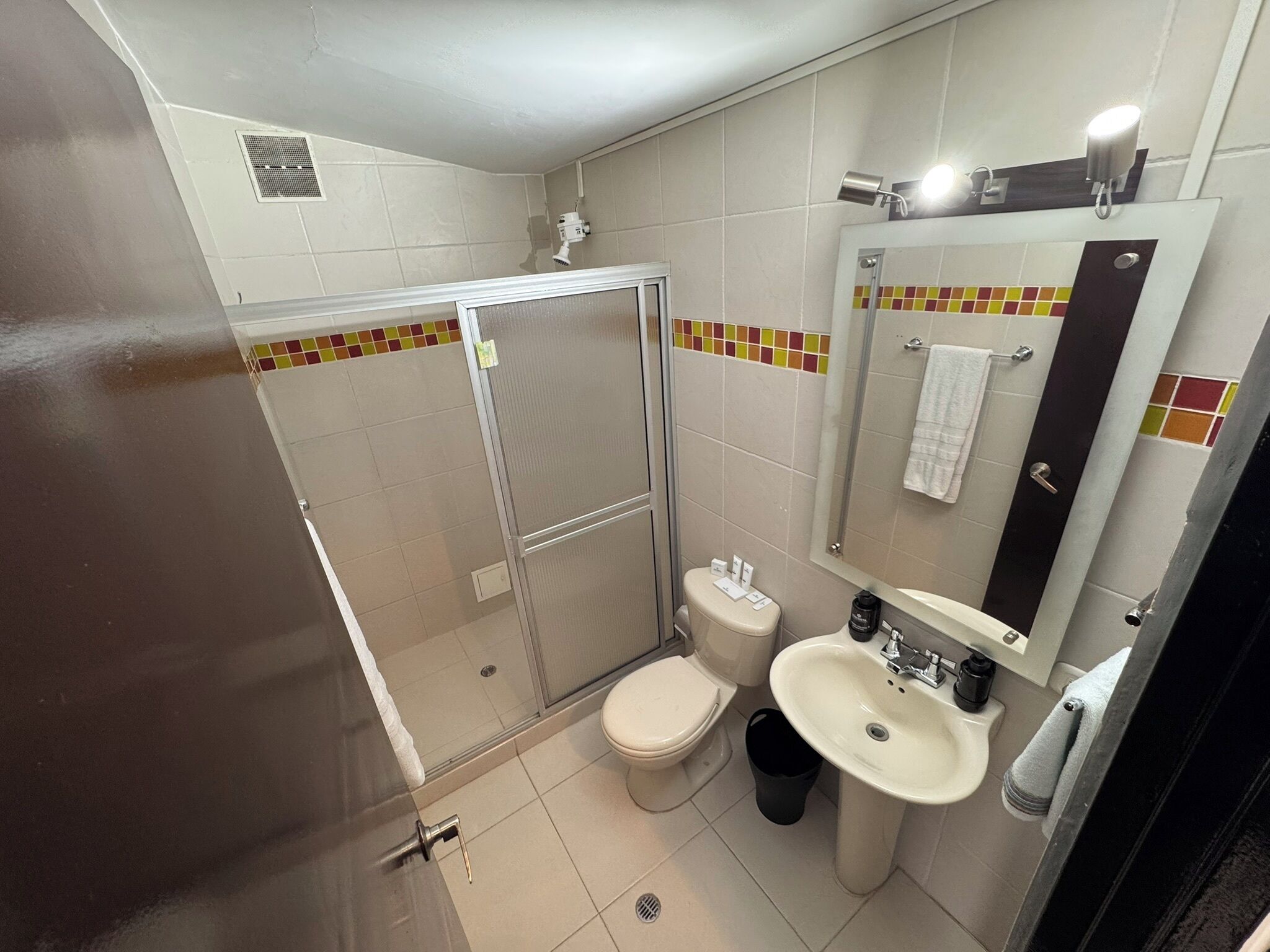 A bathroom with a shower, toilet, sink, and a mirror with a towel hanging on it.