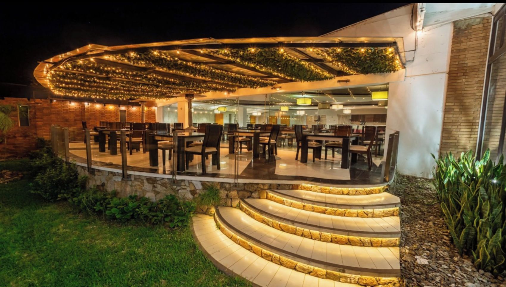 A restaurant with outdoor seating, a stone staircase, and a covered area with string lights.