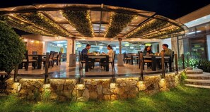 An outdoor dining area with stone walls and tables, surrounded by greenery and covered by a pergola. - D'Acosta Hotel Belencito (Nobsa)