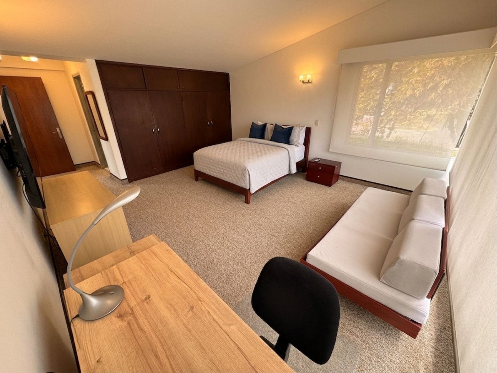 Een slaapkamer met een bed, bureau, stoel, kledingkast en raam.
