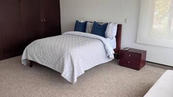 Un dormitorio con cama, mesita de noche, armario y ventana.