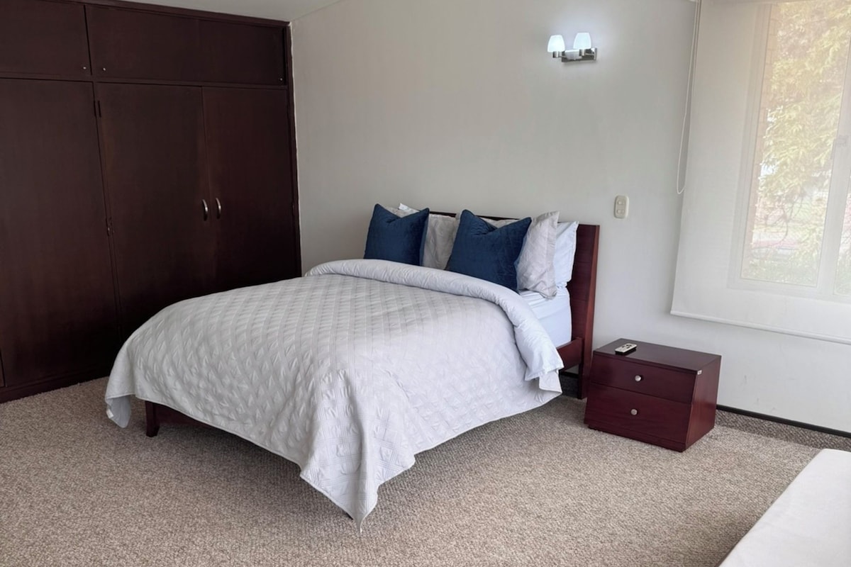 A bedroom with a bed, a wardrobe, a bedside table, and a window.
