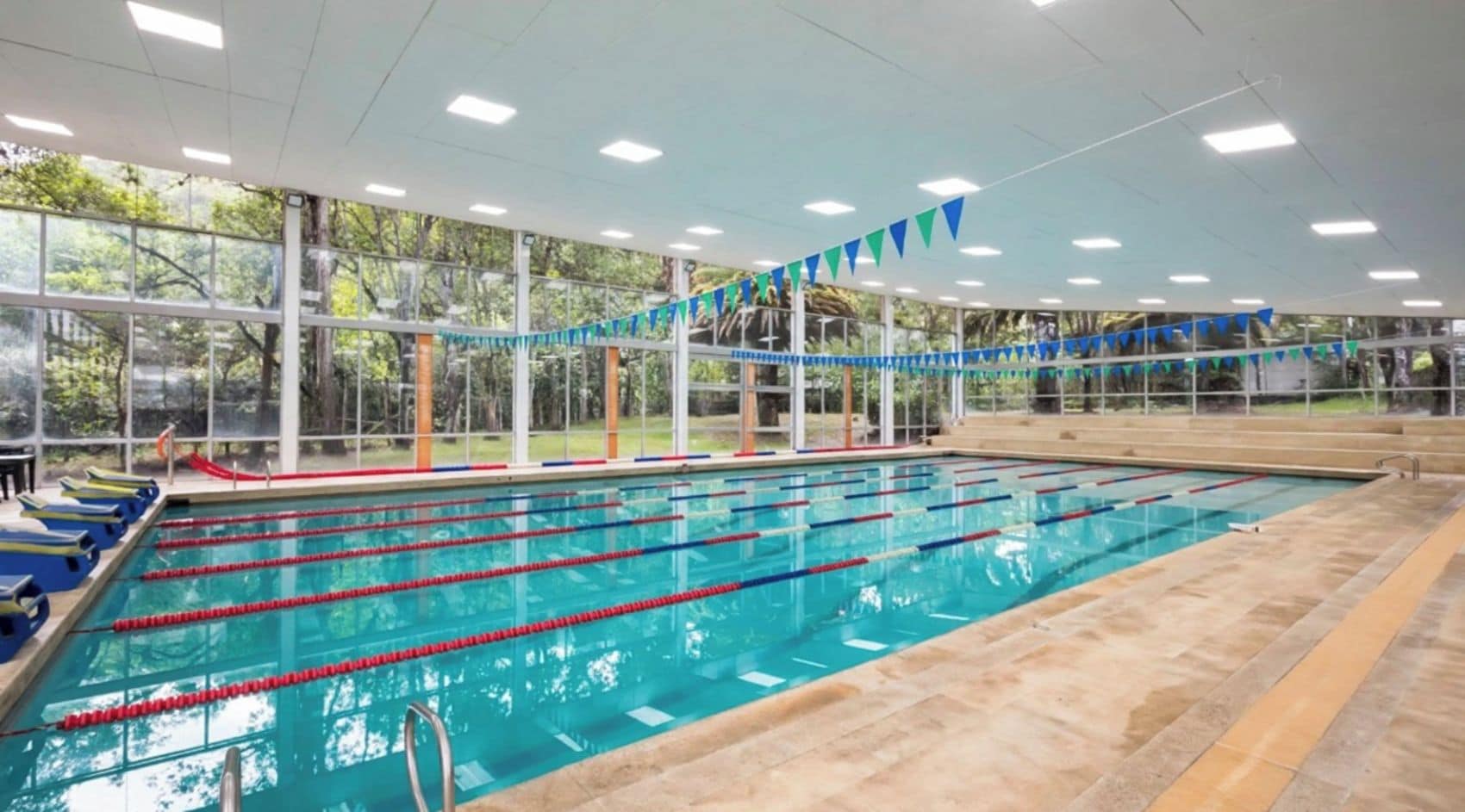 An indoor swimming pool with multiple lanes, large windows, and a tiled floor.