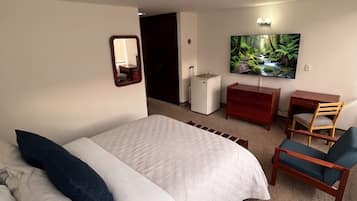 Habitación de hotel con cama, escritorio, silla, televisión y puerta que conduce a otra habitación.