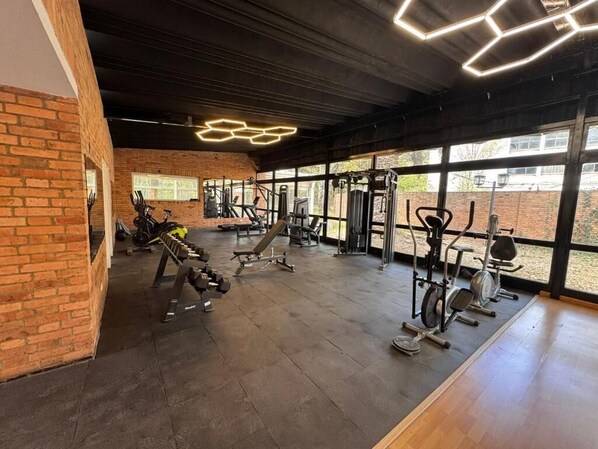 Une salle de sport équipée de divers appareils d’exercice, dotée de grandes fenêtres et d’un mur en briques.