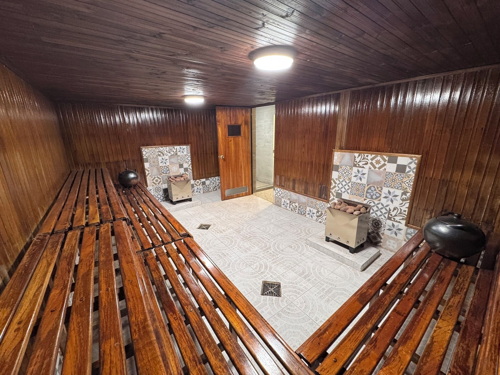 Un sauna avec des bancs en bois, des murs carrelés et une porte en bois.