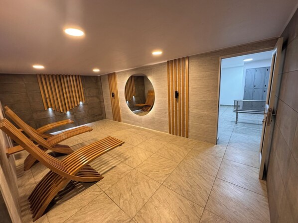 A modern spa room with wooden loungers, a circular mirror, and a view of lockers. - D'Acosta Hotel Belencito (Nobsa)
