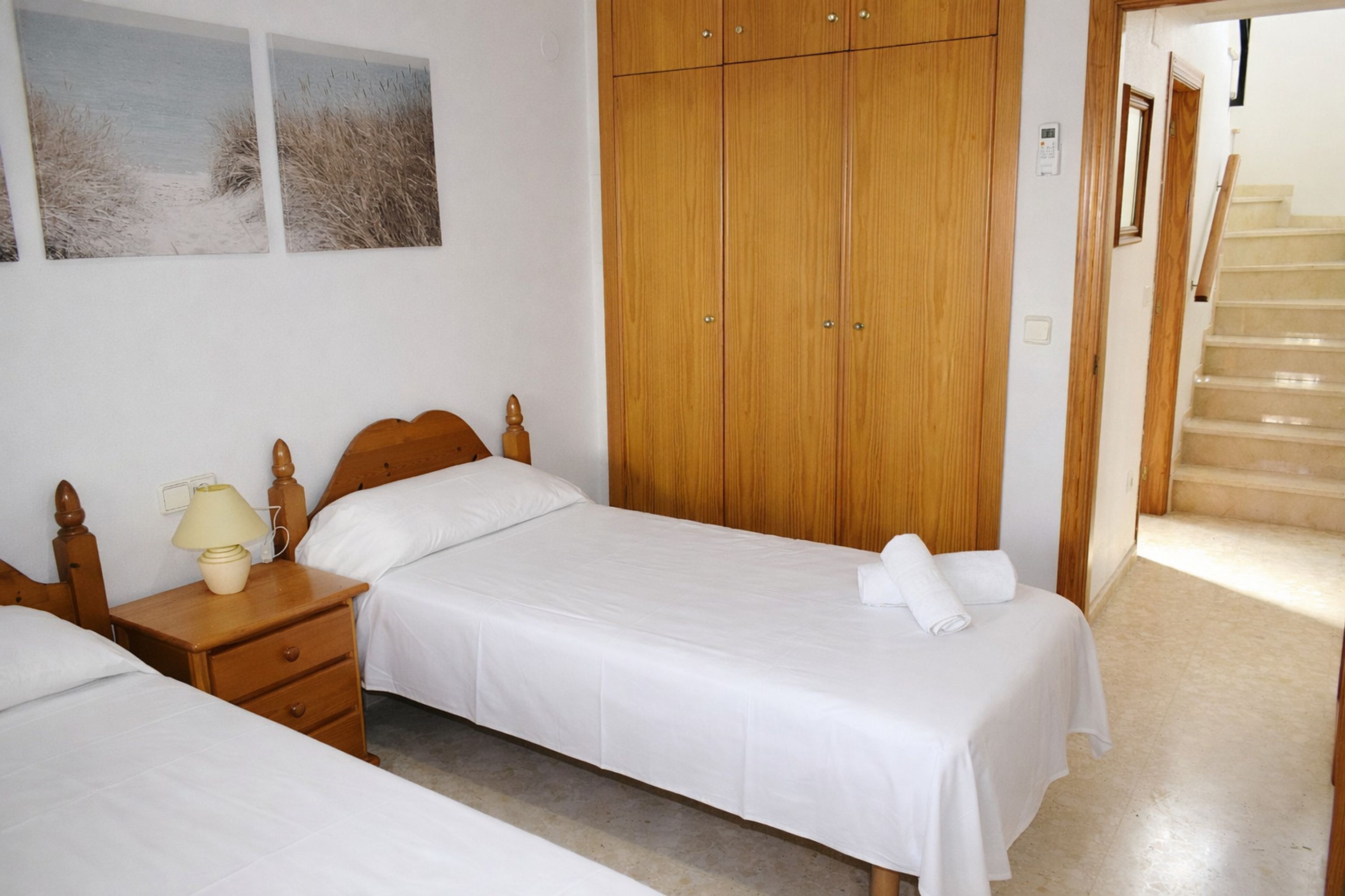 A bedroom with two beds, wooden wardrobe, and a staircase.