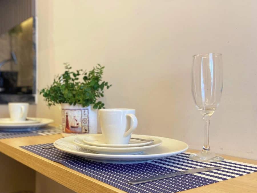 A dining area with a wooden table set with plates, cups, and a glass. A potted plant is on the wall behind the table.