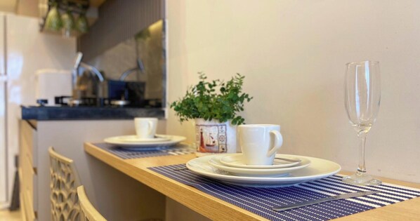 Un coin repas avec une table en bois, mise avec des assiettes, des tasses et un verre. Une plante en pot est accrochée au mur derrière la table.