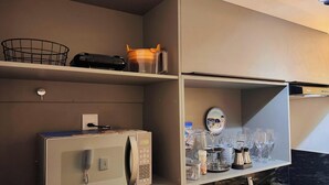Una cocina con microondas, cafetera y una repisa con cristalería.