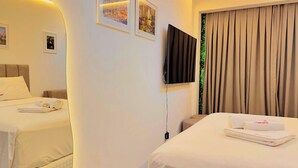 Habitación de hotel con dos camas, un televisor de pantalla plana en la pared y una ventana con cortinas.