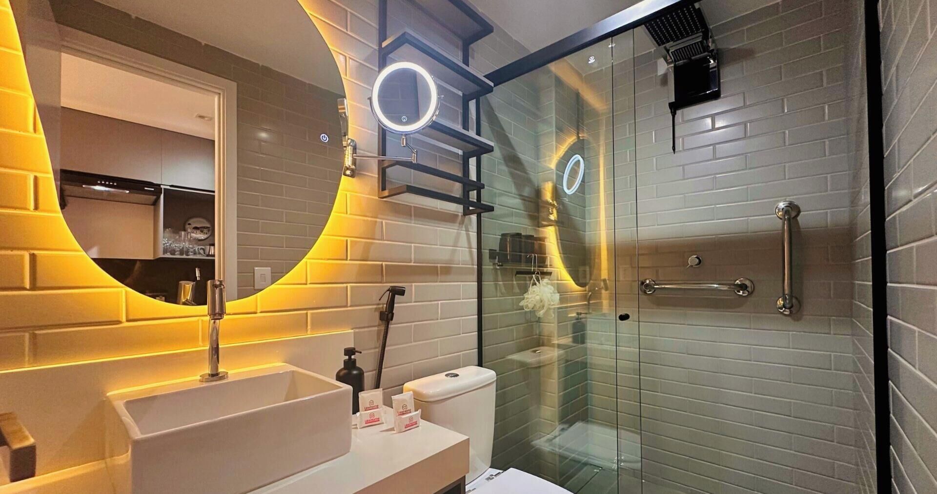 Casa de banho moderna com cabine de duche em vidro, toucador com lavatório e espelho iluminado por luz circular.