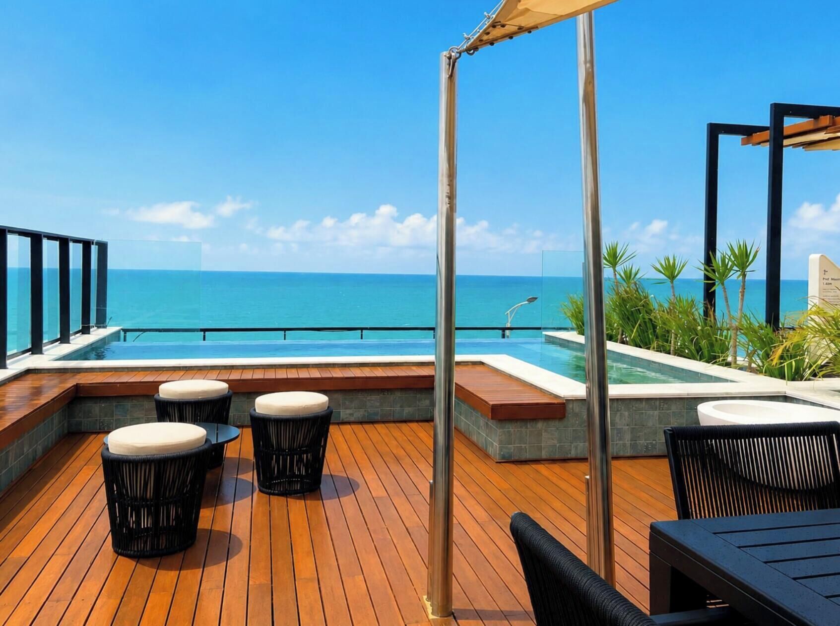 Um deck de madeira com piscina e área de estar com vista para o oceano.