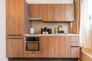 A modern kitchen with wooden cabinetry, a built-in oven, a coffee maker, and a kettle on the countertop. - Sublime appartement 2CHM / 2SDB - Saint Germain (Paris)
