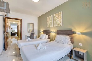 A hotel room with two beds, a desk, a chair, and a mirror. There are wall-mounted lights and a power outlet on the nightstand. - Swieqi, Central 3BR Home w/Fast WIFI & Comfort (Swieqi)