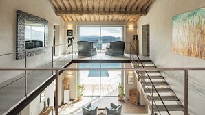 Un interior espacioso con techo alto, una escalera que conduce a un nivel superior y un gran ventanal con vistas al exterior.