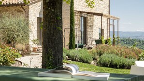 Un edificio de piedra con jardín, un árbol y un libro sobre una mesa.