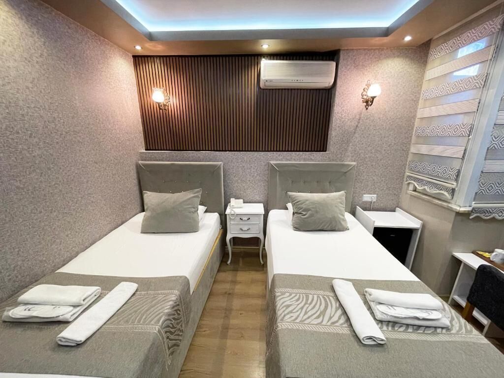 Habitación de hotel con dos camas, una mesita de noche, un equipo de aire acondicionado y una pared con diseño.