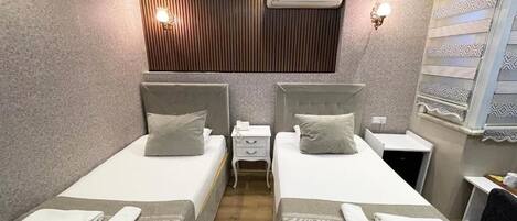 Habitación de hotel con dos camas, una mesita de noche, un equipo de aire acondicionado y una pared con diseño.