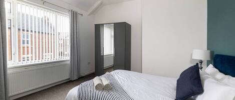 Habitación de hotel con cama, un ventanal con persianas, un radiador y un espejo.