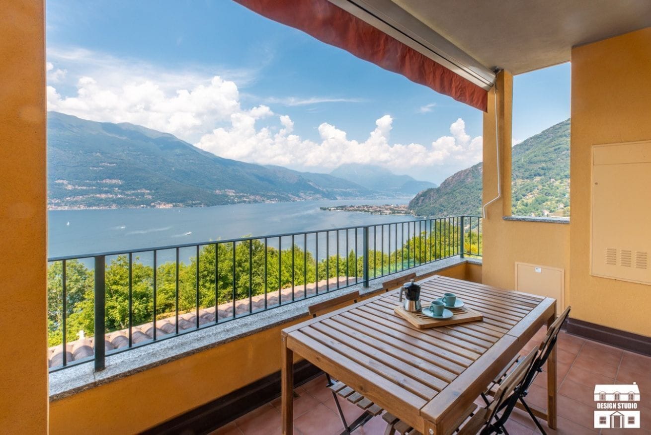 A balcony with a wooden table and chairs, overlooking a lake and mountains.