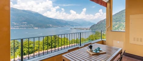 A balcony with a wooden table and chairs, overlooking a lake and mountains.